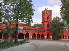 बरेली कॉलेज की लाल रंग की इमारत, घंटाघर और सामने पेड़ों से घिरा रास्ता