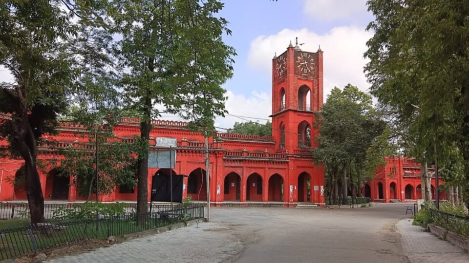 बरेली कॉलेज की लाल रंग की इमारत, घंटाघर और सामने पेड़ों से घिरा रास्ता