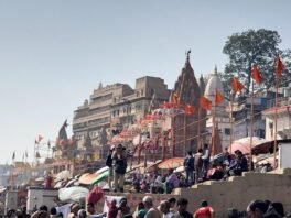 वाराणसी के दशाश्वमेध घाट पर श्रद्धालुओं की भीड़ और पीछे मंदिर व झंडे