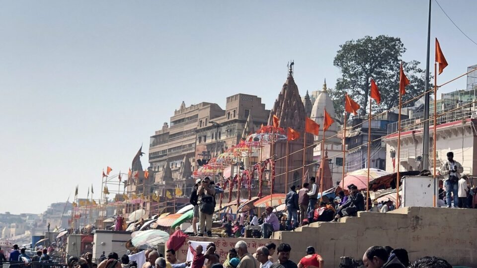 वाराणसी के दशाश्वमेध घाट पर श्रद्धालुओं की भीड़ और पीछे मंदिर व झंडे