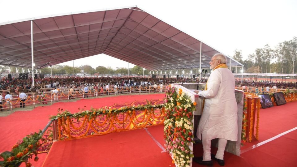 वाराणसी में मार्च 2018 की जनसभा में मंच पर संबोधित करते प्रधानमंत्री नरेंद्र मोदी और सामने बैठे लोग
